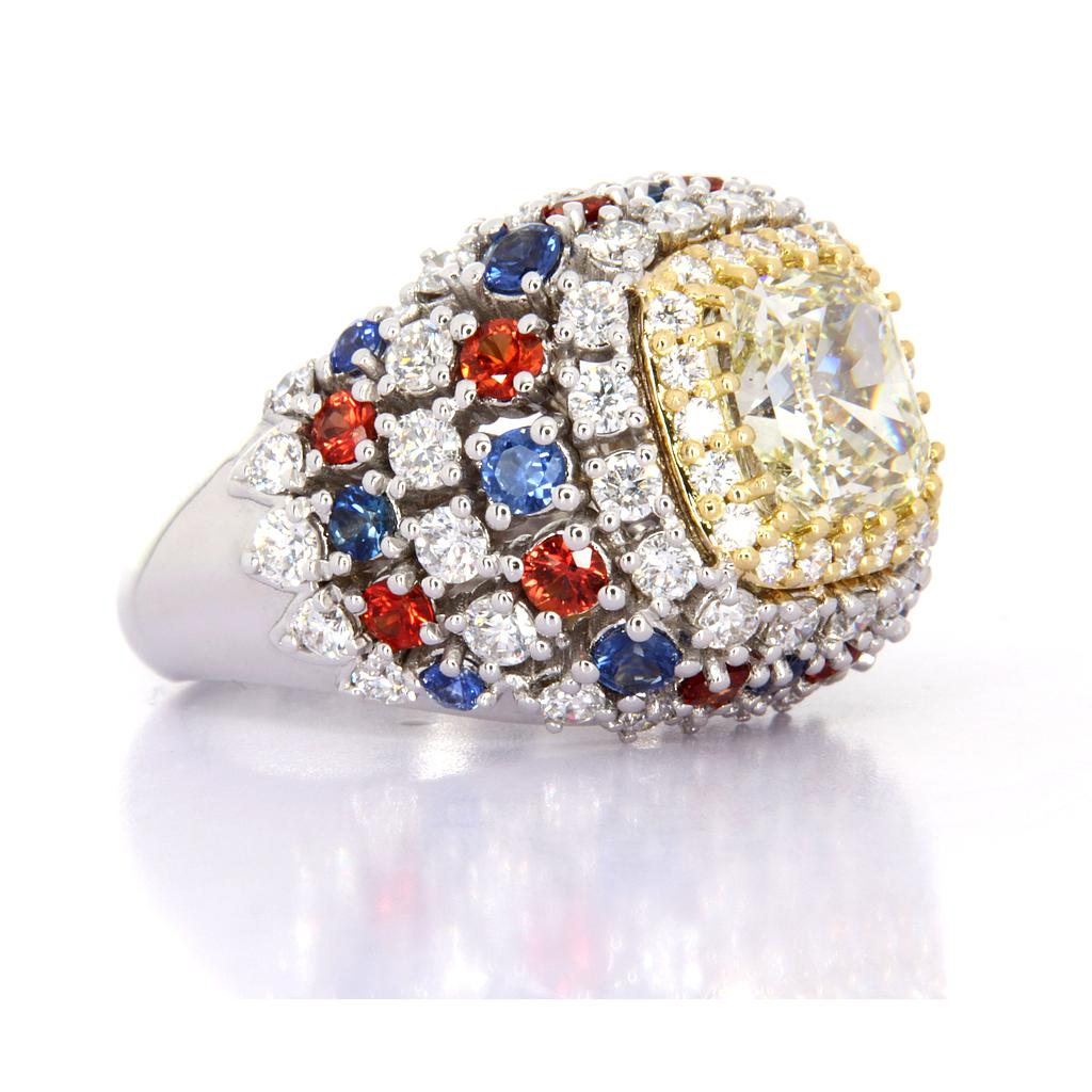 Anello in oro bianco e giallo 18 kt. con diamante cushion centrale, zaffiri blu e zaffiri fancy.
